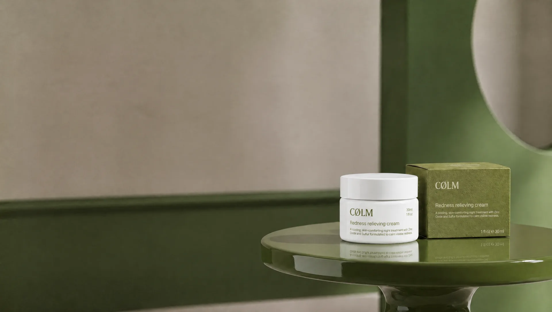 CØLM Redness Relieving Cream og dens olivengrønne æske på et grønt bord